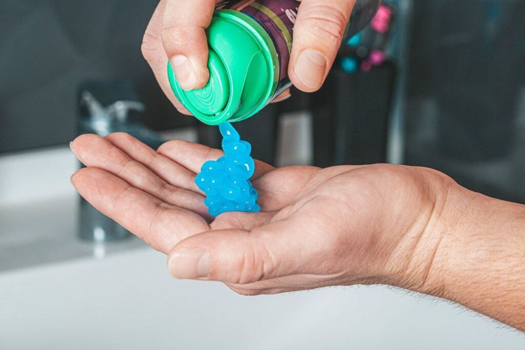 Blaues Zahngel wird aus einer Tube in die geöffnete Hand gegeben.