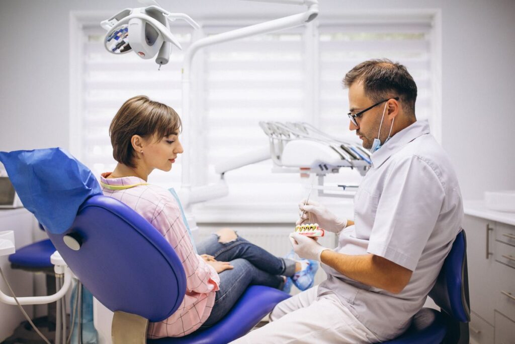 Zahnarzt erklärt einer Patientin im Behandlungsstuhl ein Gebissmodell.