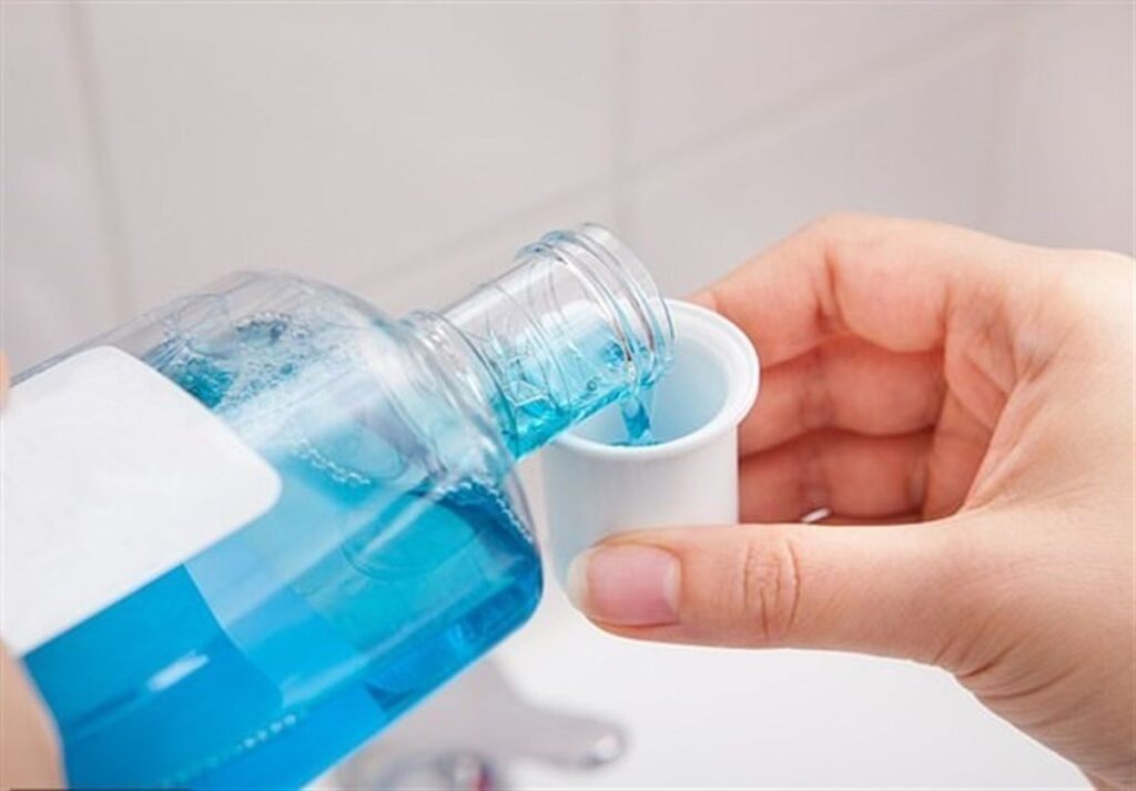 Blaues Mundwasser wird aus der Flasche in den Messbecher gegossen.